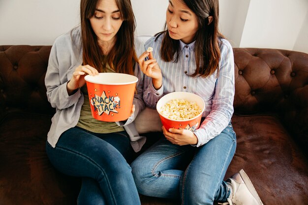 Mujeres bonitas comiendo palomitas de maíz en el sofá