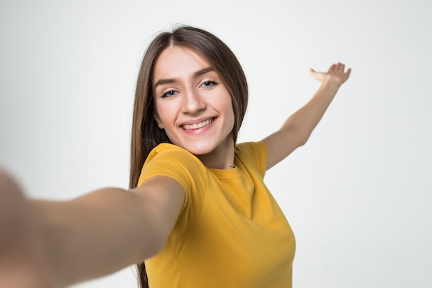 Mujeres bonitas jovenes que toman el selfie en el teléfono celular aislado en la pared blanca