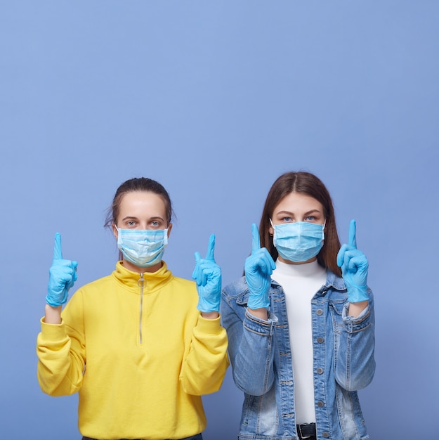 Mujeres bonitas con máscaras médicas y guantes de látex señalando con el dedo índice