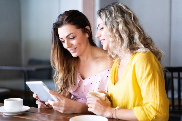 Mujeres bonitas navegando en la computadora de la tableta y tomando café