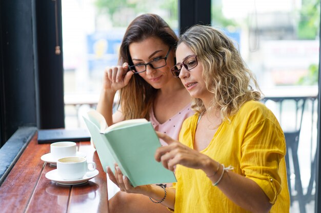 Mujeres bonitas que leen el libro de texto y que beben el café en café