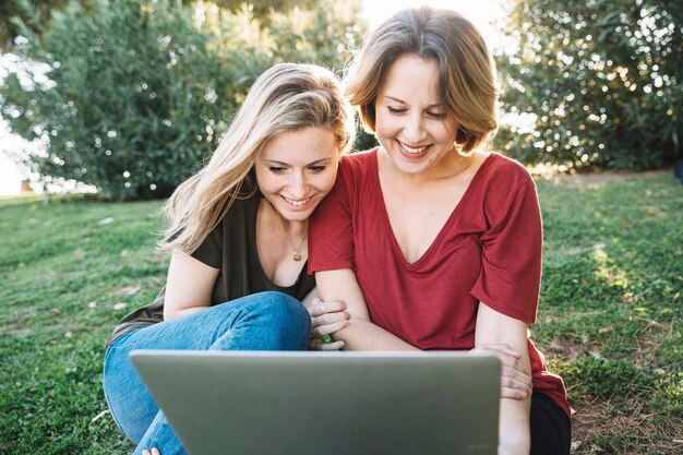 Mujeres bonitas que navegan la computadora portátil en la tierra