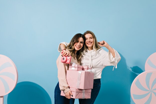 Mujeres bonitas con regalos abrazando en pared azul