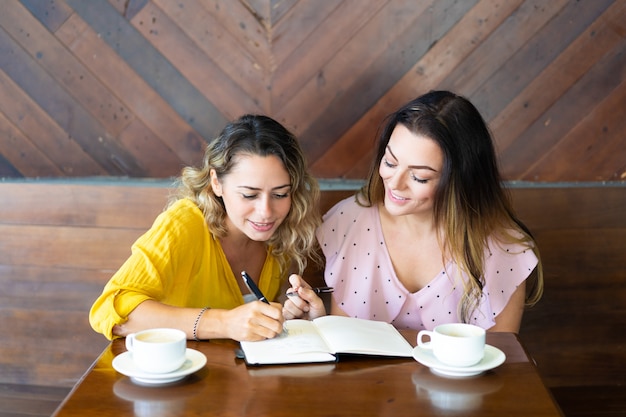 Mujeres bonitas tomando café y tomando notas en el café