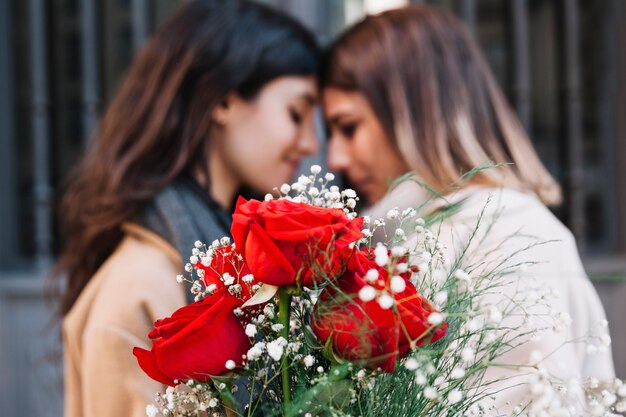 Mujeres cariñosas con rosas a punto de besarse