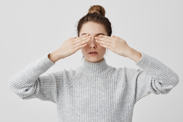 Mujeres caucásicas adultas de 30 años con el pelo en moño que cubre los ojos con ambas manos. Chica concentrada esperando sorpresa con los ojos cerrados, no sabe qué esperar. Lenguaje corporal