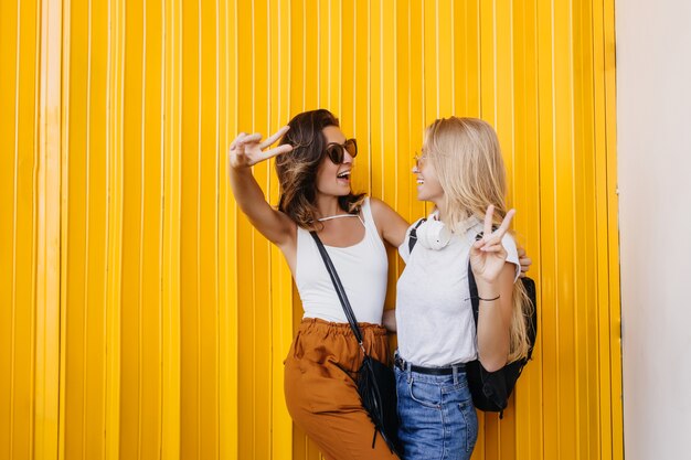 Mujeres caucásicas positivas mirándose durante la sesión de fotos sobre fondo amarillo.