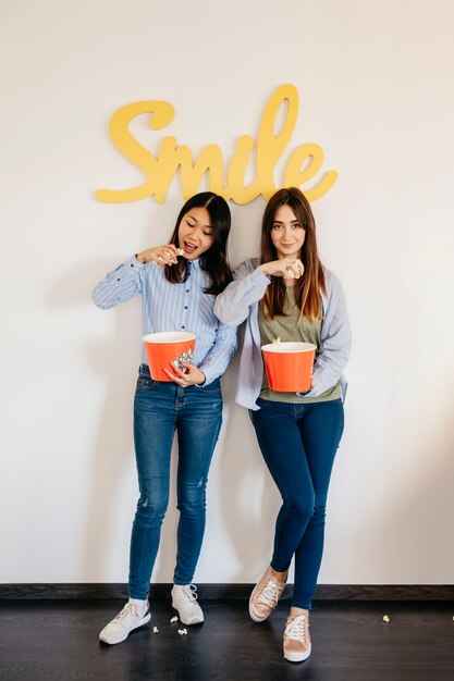 Mujeres comiendo palomitas de maíz cerca de la escritura de sonrisa