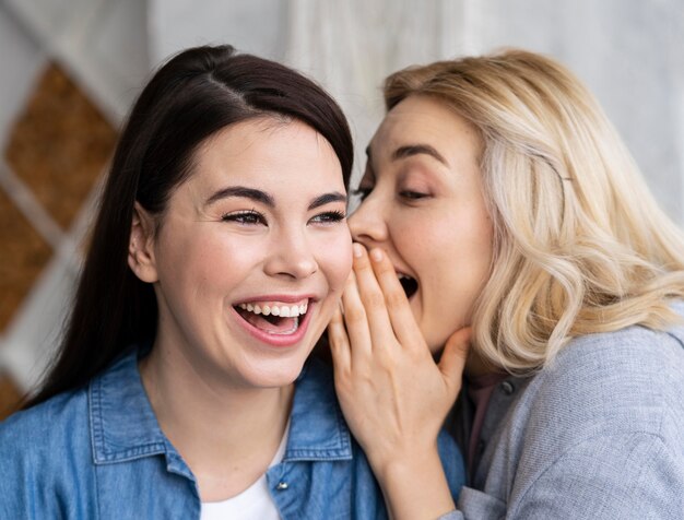 Mujeres contando un secreto y riendo