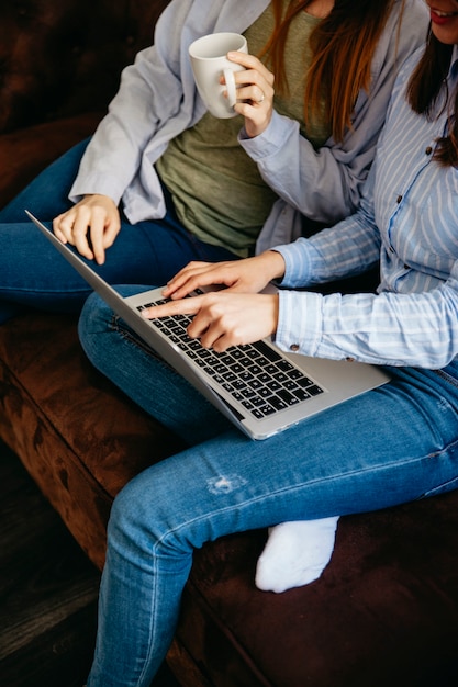 Mujeres de cultivos usando la computadora portátil en el sofá