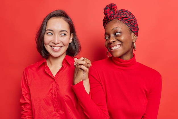 Foto gratuita las mujeres se dan la mano juntas, siendo mejores amigos, se reconcilian entre sí después de la pelea, sonríen alegremente aisladas en rojo brillante.