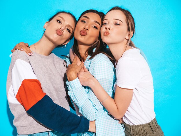 Mujeres despreocupadas atractivas que presentan cerca de la pared azul en estudio. Modelos positivos divirtiéndose y abrazándose. Hacen cara de pato