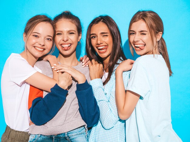 Mujeres despreocupadas atractivas que presentan cerca de la pared azul en estudio. Modelos positivos divirtiéndose y abrazándose. Muestran lenguas