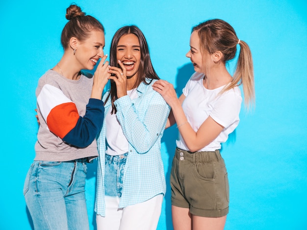 Mujeres despreocupadas atractivas que presentan cerca de la pared azul en estudio. Modelos positivos divirtiéndose y abrazándose