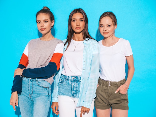 Mujeres despreocupadas atractivas que presentan cerca de la pared azul en estudio. Modelos positivos divirtiéndose y abrazándose