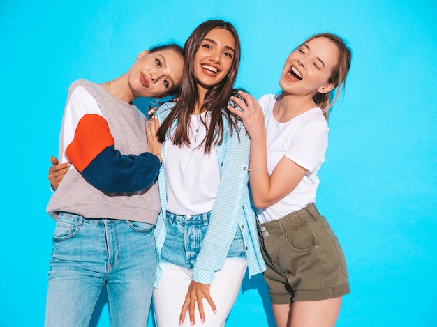 Mujeres despreocupadas atractivas que presentan cerca de la pared azul en estudio. Modelos positivos divirtiéndose y abrazándose