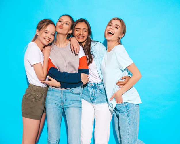 Mujeres despreocupadas atractivas que presentan cerca de la pared azul en estudio. Modelos positivos divirtiéndose y abrazándose