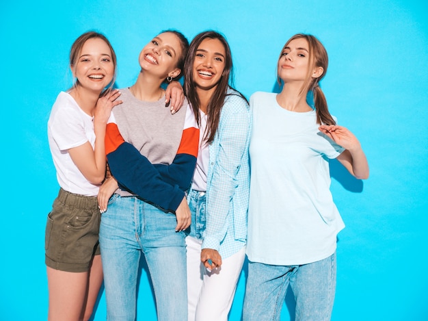 Mujeres despreocupadas atractivas que presentan cerca de la pared azul en estudio. Modelos positivos divirtiéndose y abrazándose