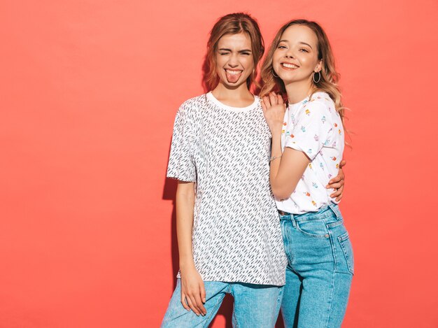 Mujeres despreocupadas atractivas que presentan la pared azul rosada. Modelos positivos divirtiéndose y mostrando lengua