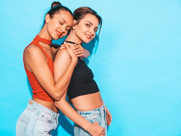 Mujeres despreocupadas sexy posando junto a la pared azul en el estudio. Modelos positivos divirtiéndose.