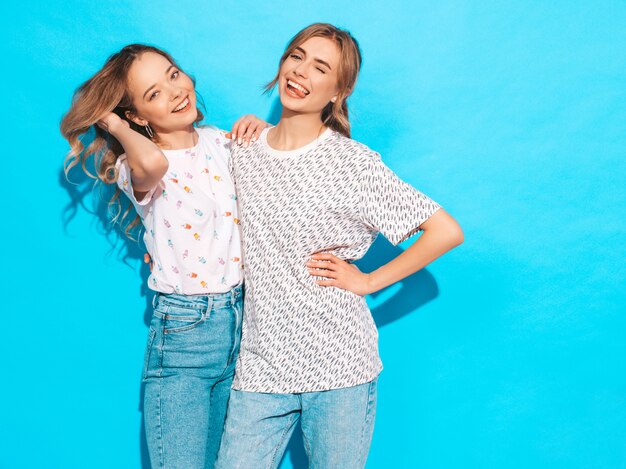 Mujeres despreocupadas sexy posando junto a la pared azul. Modelos positivos divirtiéndose. Guiña y muestra la lengua