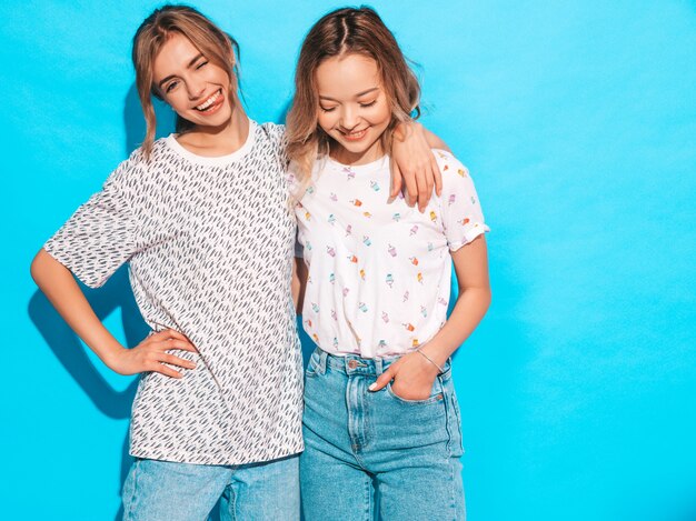 Mujeres despreocupadas sexy posando junto a la pared azul. Modelos positivos divirtiéndose. Guiña y muestra la lengua