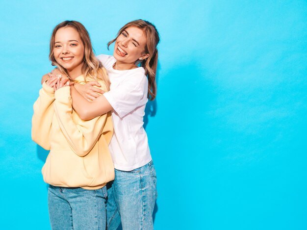 Mujeres despreocupadas sexy posando junto a la pared azul. Modelos positivos divirtiéndose y mostrando lengua