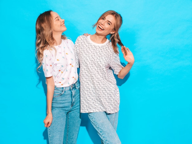 Mujeres despreocupadas sexy posando junto a la pared azul. Modelos positivos divirtiéndose