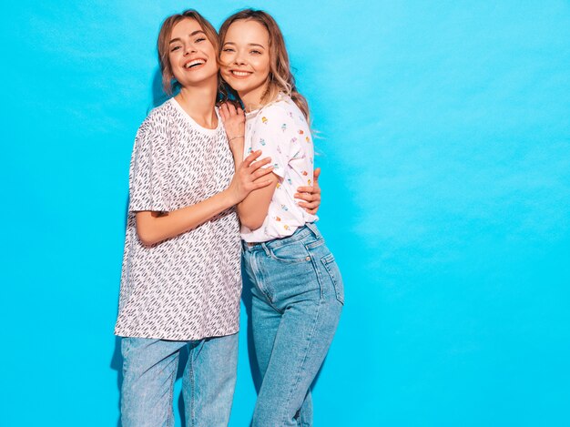 Mujeres despreocupadas sexy posando junto a la pared azul. Modelos positivos divirtiéndose