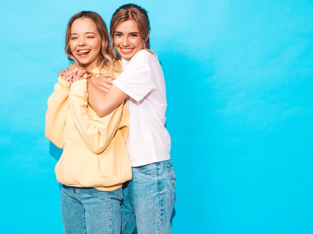 Mujeres despreocupadas sexy posando junto a la pared azul. Modelos positivos divirtiéndose