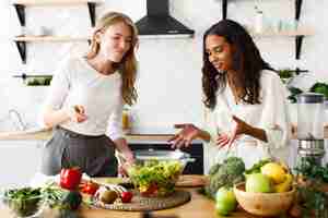 Foto gratuita las mujeres de diferentes nacionalidades están hablando y comiendo una ensalada en la cocina.