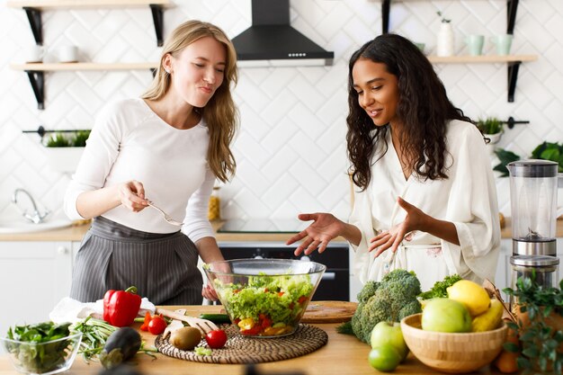 Las mujeres de diferentes nacionalidades están hablando y comiendo una ensalada en la cocina.