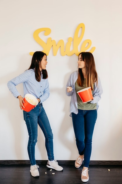 Mujeres divertidas con palomitas de maíz cerca de la escritura de la sonrisa