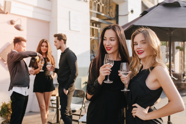 Mujeres elegantes discutiendo algo mientras beben champán en la calle