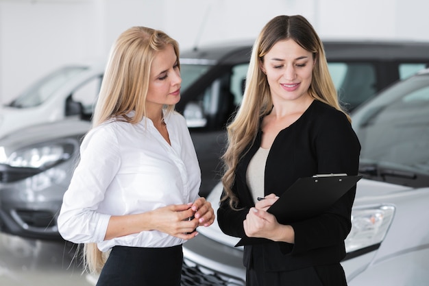 Foto gratuita mujeres elegantes discutiendo en la sala de exposición de automóviles