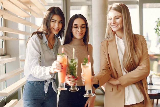 Mujeres elegantes de pie en un café y bebiendo un cóctel
