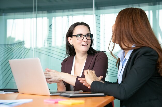 Mujeres empresarias alegres emocionadas discutiendo el proyecto mientras están sentados en la computadora portátil abierta