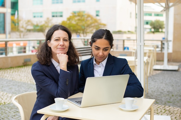 Mujeres empresarias felices con laptop en café al aire libre
