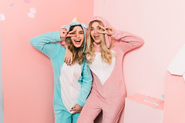 Mujeres encantadoras en kigurumi de pie en la pared rosa