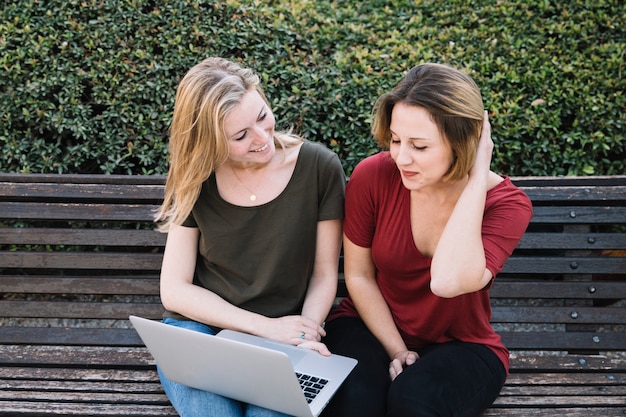 Mujeres encantadoras que usan la computadora portátil en el parque