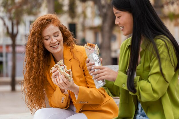 Mujeres felices comiendo juntos comida callejera