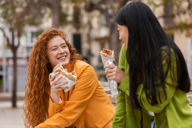 Mujeres felices comiendo juntos comida callejera