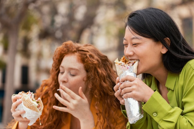 Mujeres felices comiendo juntos comida callejera