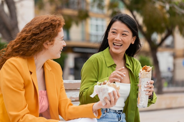 Mujeres felices comiendo juntos comida callejera