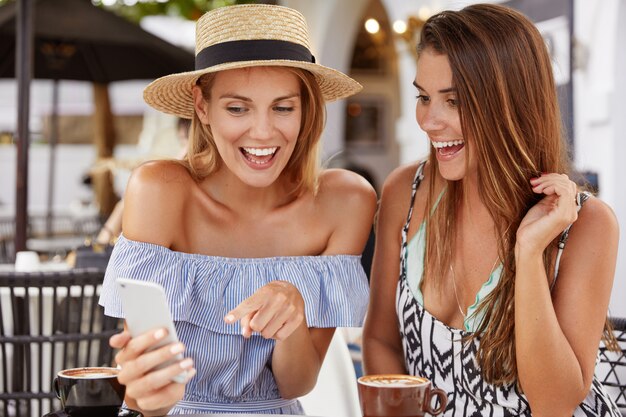 Las mujeres felices positivas tienen vacaciones de verano, contentas de ver una oferta especial para turistas en el sitio web de Internet, señalan con expresión alegre en la pantalla del teléfono inteligente. Personas, ocio, concepto de tecnología.