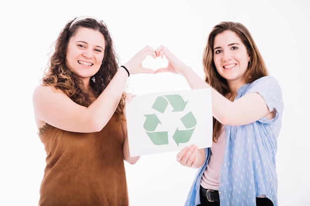 Las mujeres felices que sostienen reciclan la pancarta que hace la muestra del corazón con las manos