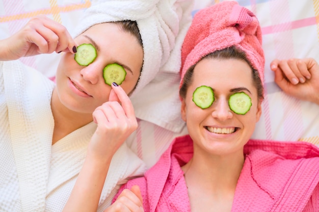 Mujeres felices con rodajas de pepino en los ojos