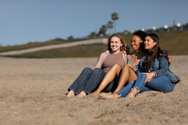 Mujeres felices de tiro completo sentadas juntas en la playa