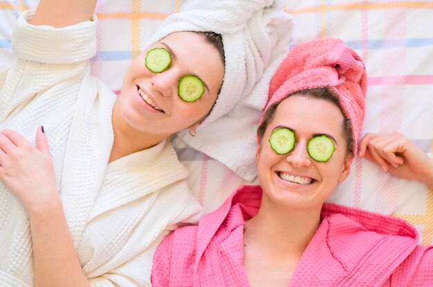 Mujeres felices con toallas en la cabeza y rodajas de pepino en los ojos