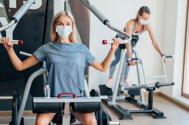 Mujeres haciendo ejercicio en el gimnasio con equipo y máscara.